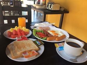 A breakfast table with plates of toast, fruit, eggs, bacon, and a cup of coffee.
