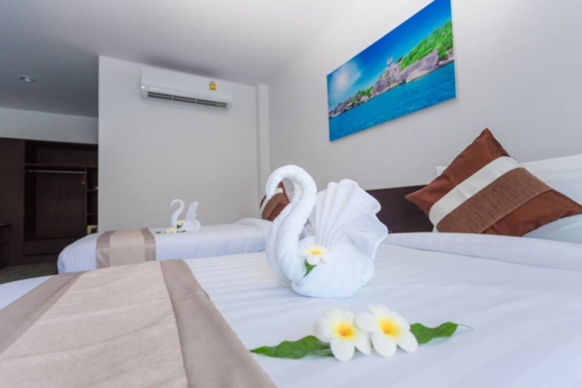 A hotel room with two beds, a painting of a coastal scene, and a swan-shaped towel on one bed.