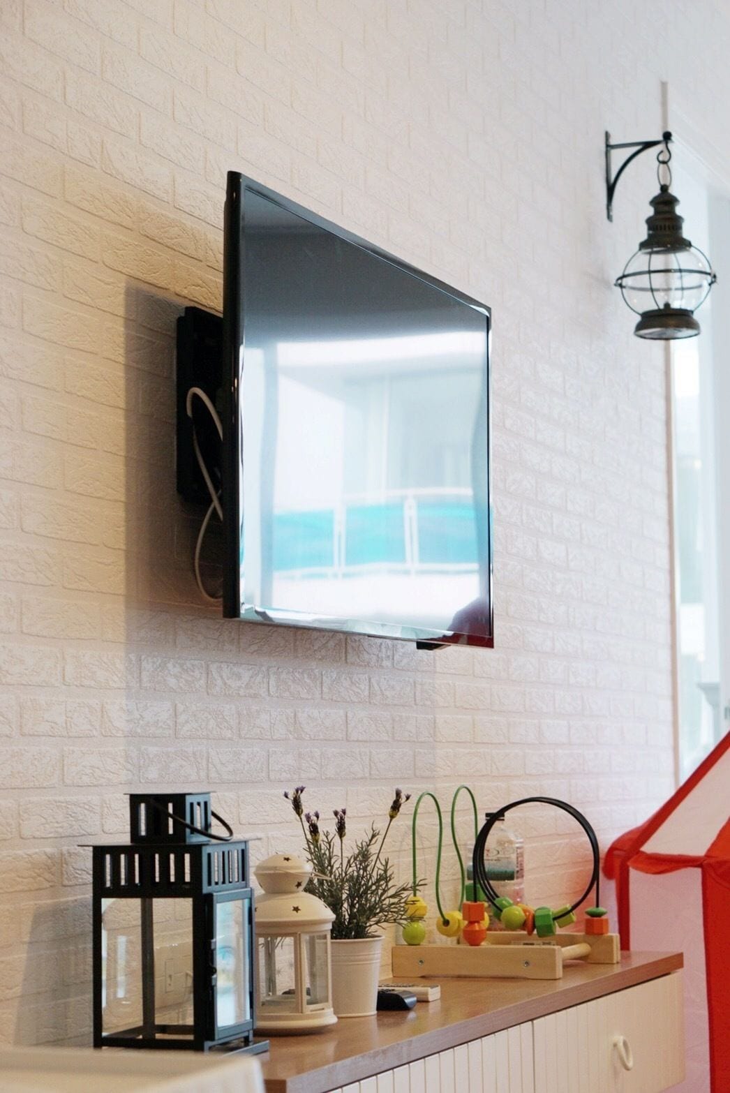 A modern kitchen with a flat-screen TV mounted on a white brick wall, a wooden countertop, and a hanging light fixture.