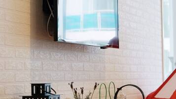 A modern kitchen with a flat-screen TV mounted on a white brick wall, a wooden countertop, and a hanging light fixture.