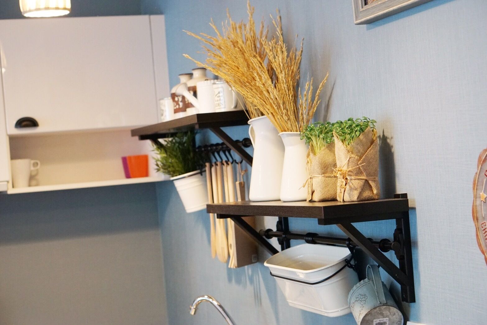 Une salle de bain avec un meuble blanc, une étagère contenant des ustensiles de cuisine, un lavabo et une horloge.
