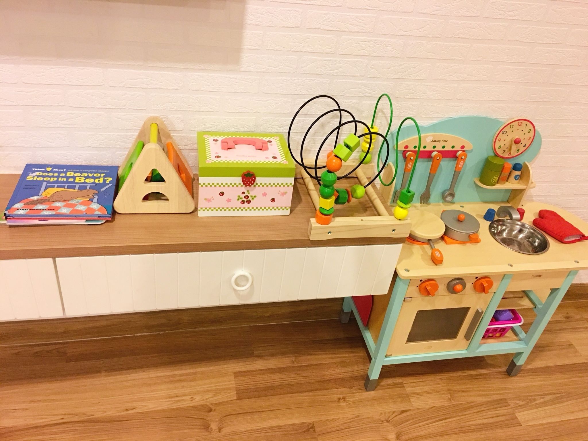 A children's play area with a wooden table, a toy kitchen set, and a book titled "Does a Beaver Sleep in a Bed?".