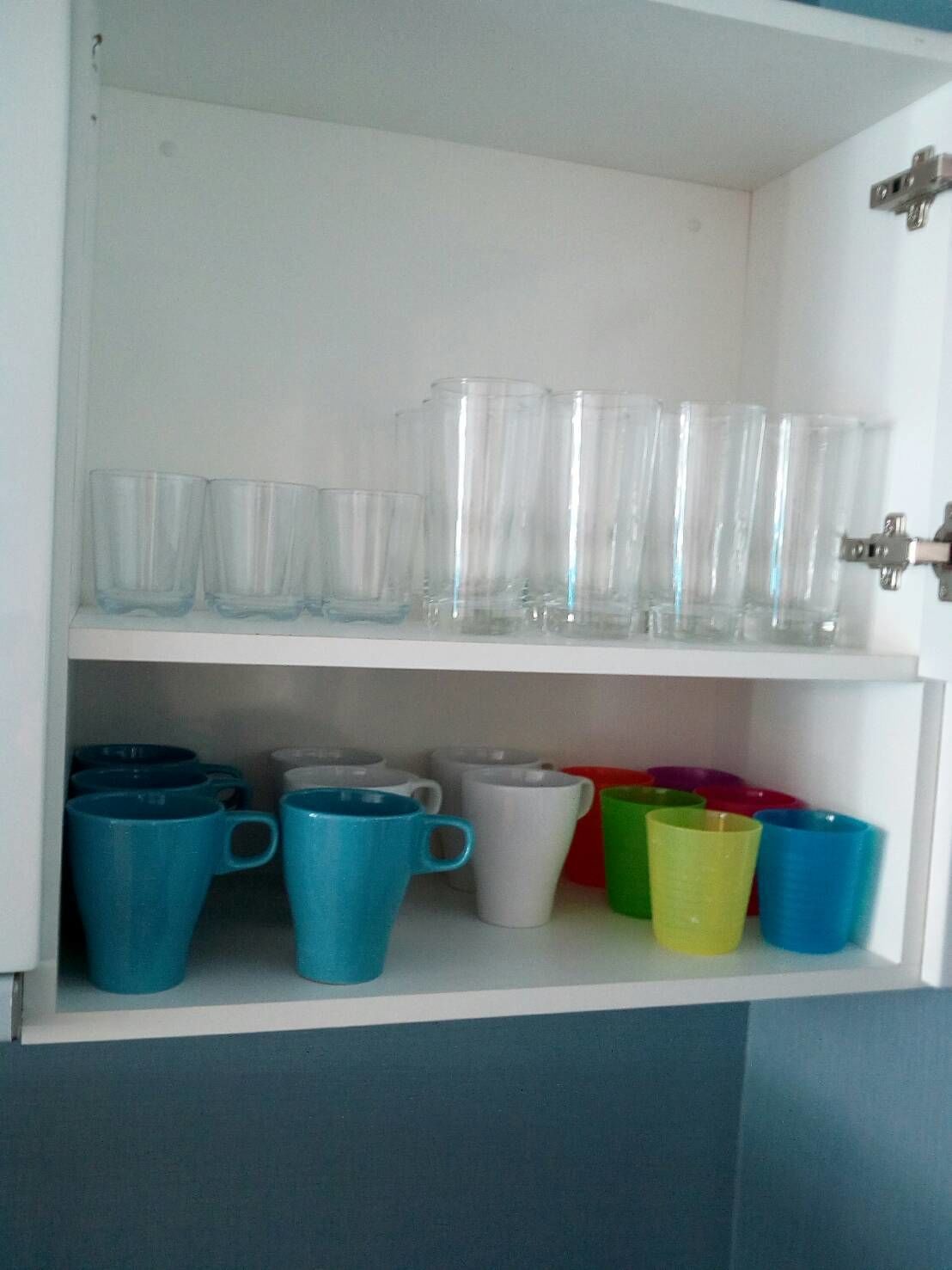 A storage cabinet with clear drinking glasses and colorful mugs.