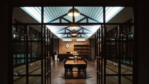 Un espace de salle à manger moderne, doté d’un plafond haut, d’une verrière et d’une table centrale entourée de chaises.