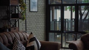 Un coin salon confortable avec un canapé en cuir, une table basse en bois et une chaise en métal. Une grande fenêtre offre une vue sur l’extérieur.