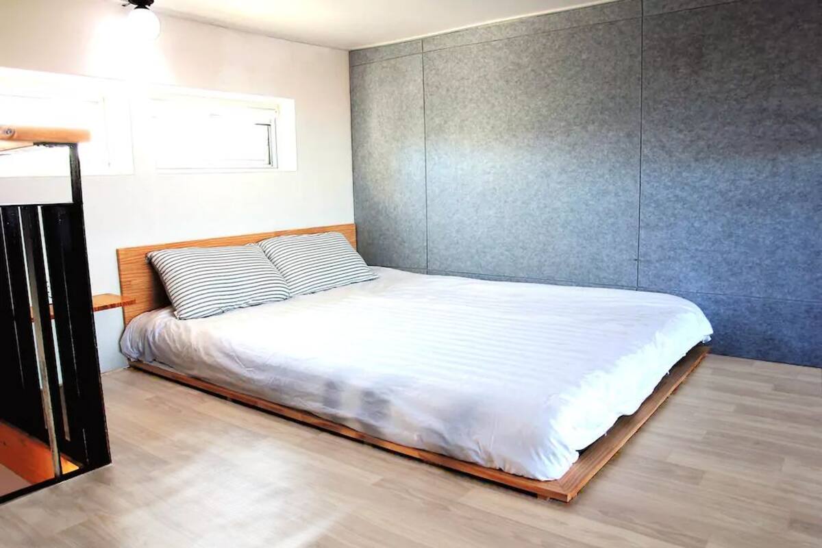 A modern bedroom with a wooden bed frame, white bedding, and a grey accent wall.