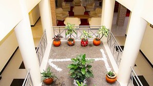 Un hall de hotel con una zona de estar central, una escalera adornada con plantas y vistas al piso superior.