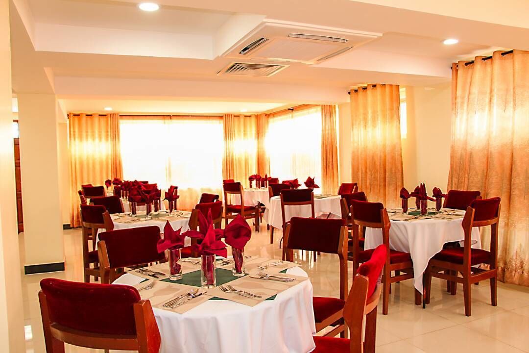 A dining area with multiple round tables, each set with red chairs and white tablecloths.