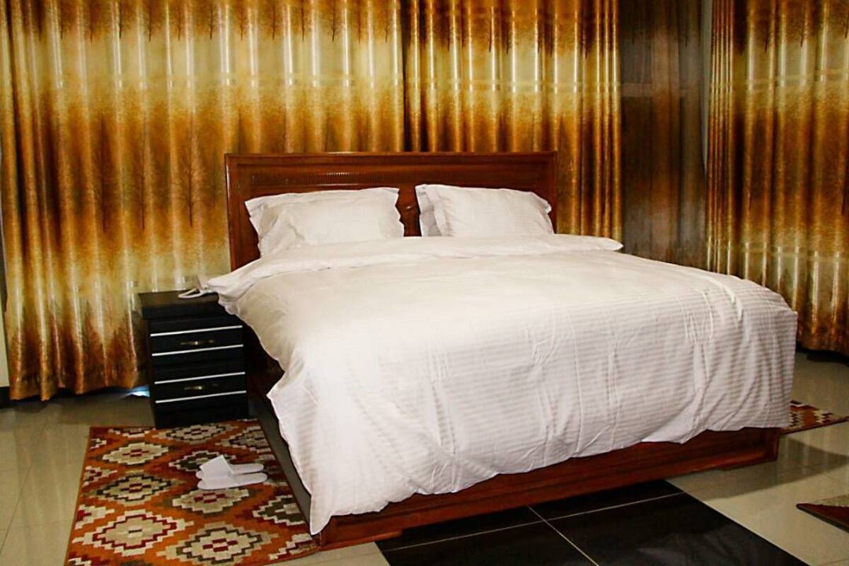 A neatly made bed with white linens in a room with a patterned rug and a wooden nightstand.