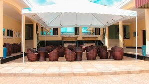 Un área de estar exterior con toldo blanco, mobiliario de mimbre y suelo de baldosas.