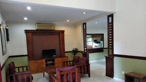 A living room with a TV, wooden furniture, and a fan.