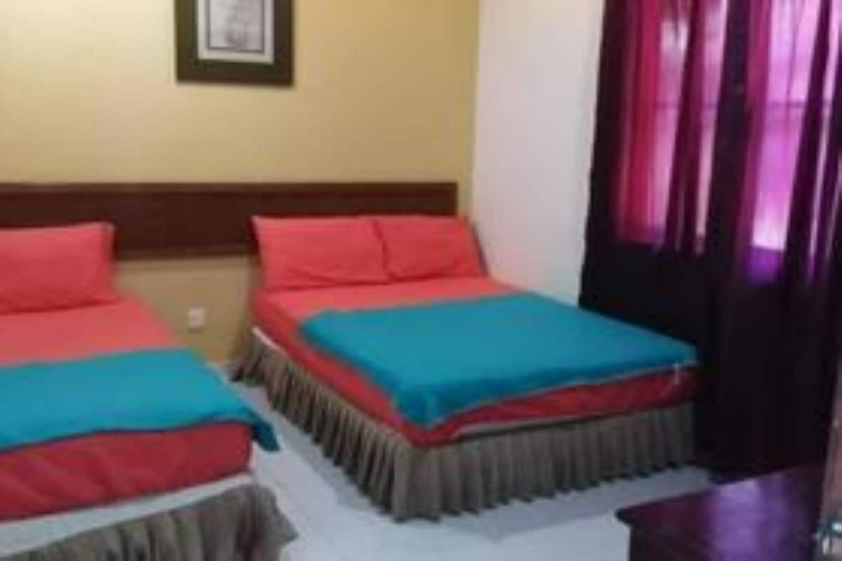 A room with two beds, each with a red and blue bedspread, a wooden headboard, and a framed picture on the wall.