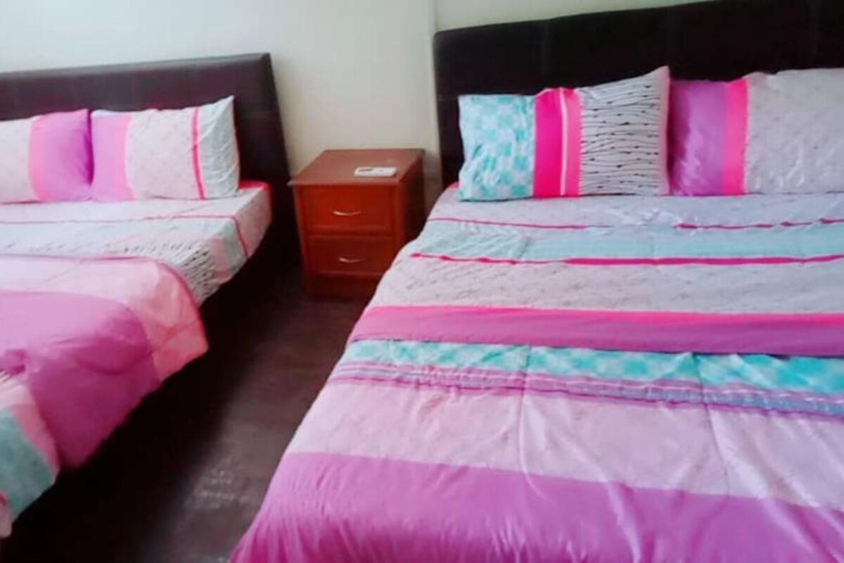 A room with two beds, each with a headboard, a nightstand, and a drawer unit.
