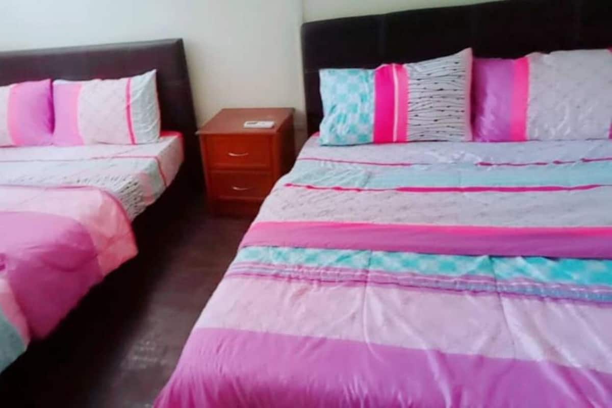 A room with two beds, each with a headboard, a nightstand, and a drawer unit.