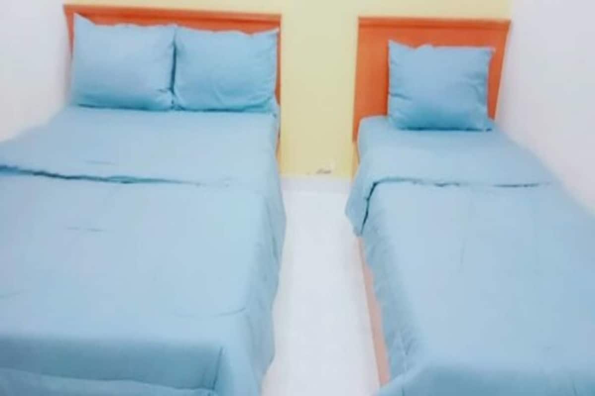 Two single beds with orange headboards and blue bedding in a room with white walls.