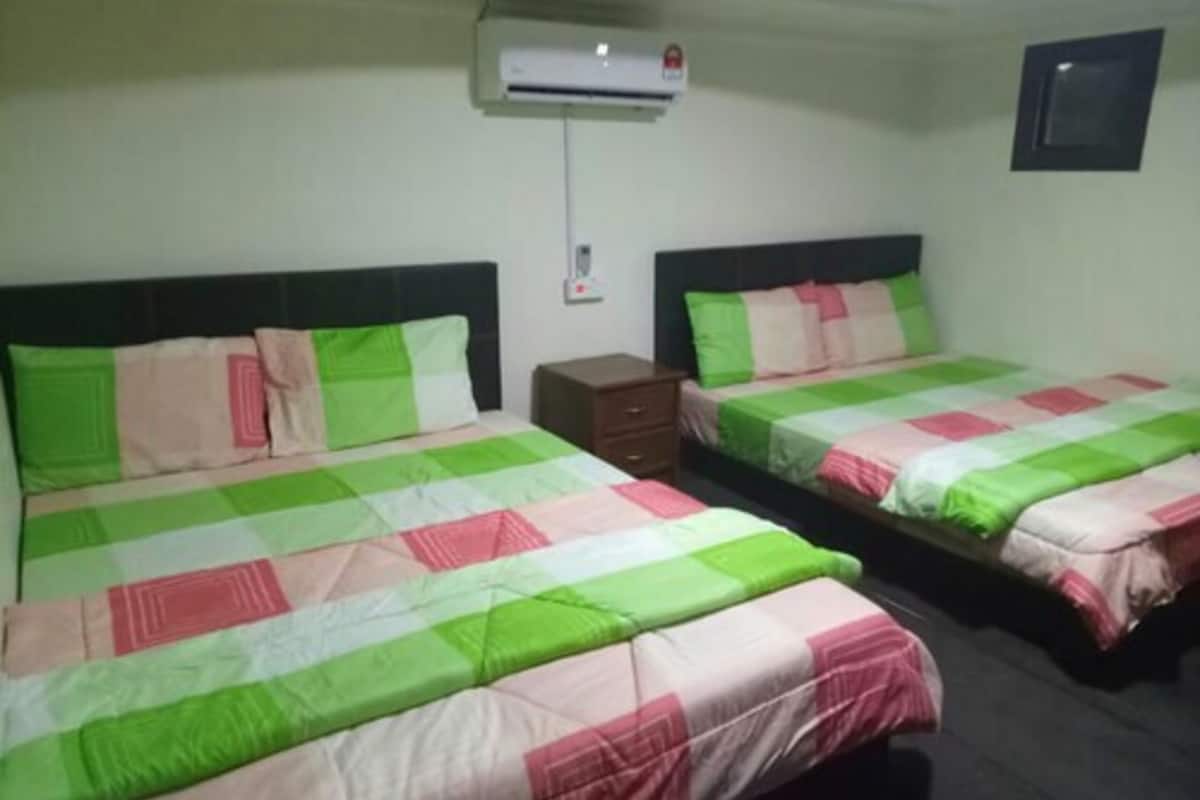 Two single beds with green and pink bedding, a small wooden nightstand, and a wall-mounted air conditioner.