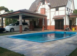 Ett hus med en swimmingpool, en täckt uteplats och en bil parkerad utanför.