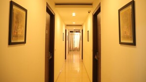 A hotel hallway with framed artwork on the walls, a tiled floor, and doors leading to rooms. - Nirvana Suites (New Delhi)