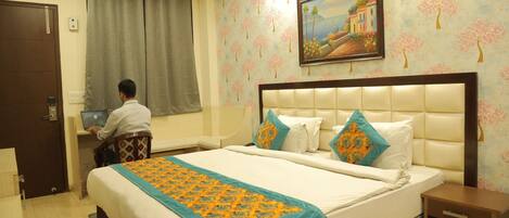A hotel room with a large bed, a desk, and a computer.