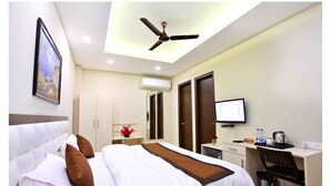 Ein Hotelzimmer mit Bett, Schreibtisch, Stuhl, Fernseher und Deckenventilator.