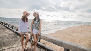 Two people walking along a concrete pier with a beach and ocean in the background. - Panwana Resort (Rayong)