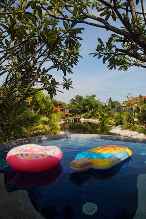 An outdoor swimming pool with two inflatable rings, surrounded by lush greenery and a view of a building in the background.