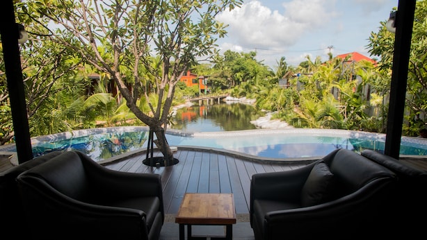 A pool area with two black leather sofas and a small wooden table, surrounded by lush greenery and a view of a bridge and buildings in the distance. - Panwana Resort (Rayong)