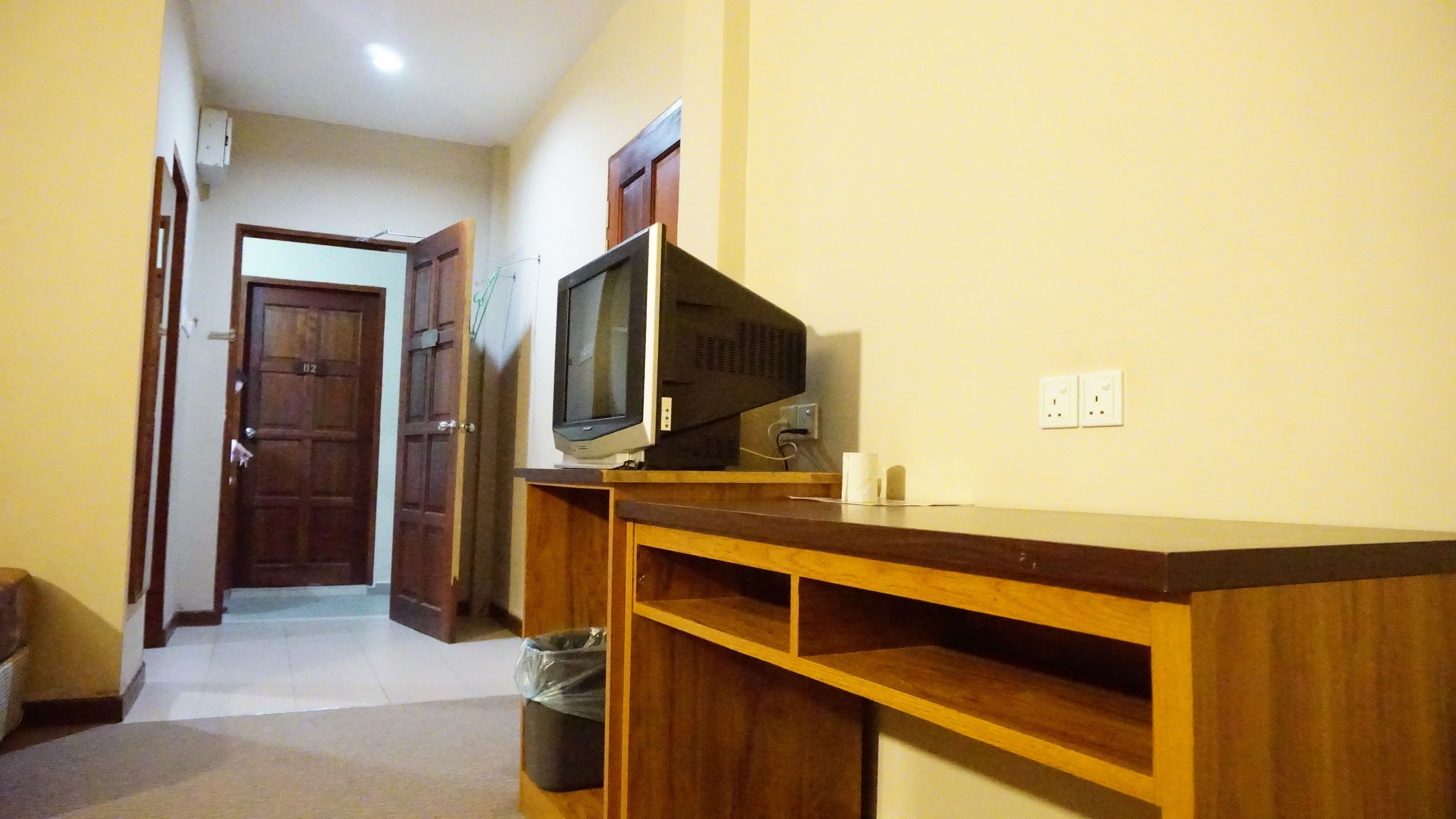 A room with a wooden TV stand, a television, and a trash bin.