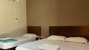 Habitación de hotel con dos camas individuales, una cama grande y un aire acondicionado instalado en la pared.