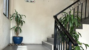 Una escalera con barandilla negra, una planta en maceta azul y un cartel que indica los números de habitación 201 al 219.