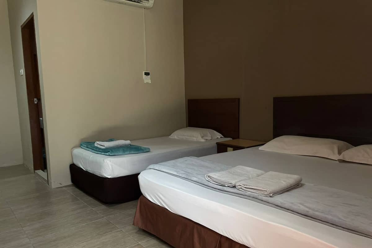 A hotel room with two beds, a wooden floor, and a small bedside table with a lamp.