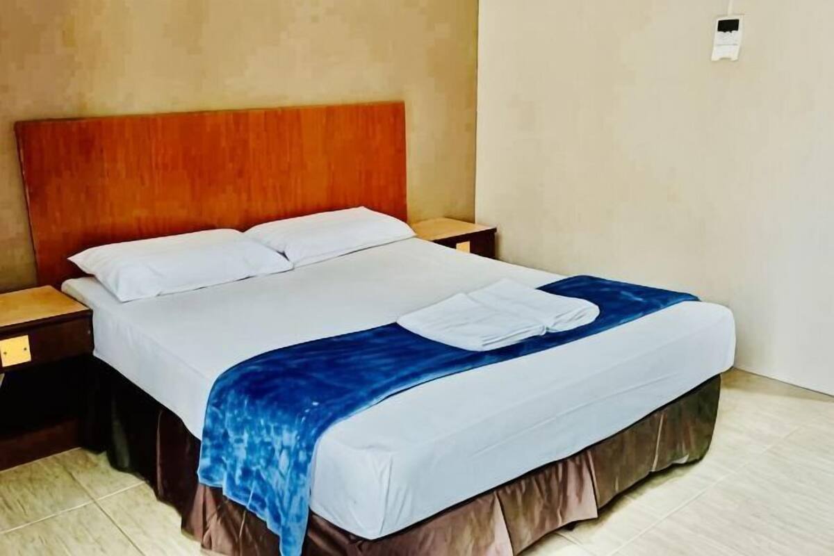 A bed with white linens, a blue blanket, and a wooden headboard.