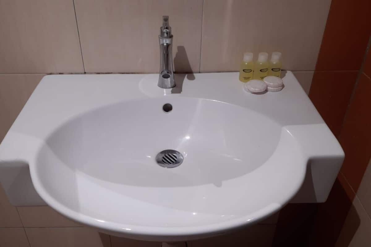 A white bathroom sink with a chrome faucet, a drain, and three bottles of lotion on the countertop.