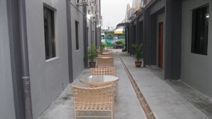 Un callejón estrecho con muebles de mimbre y plantas en macetas, que conduce a la entrada de un edificio.