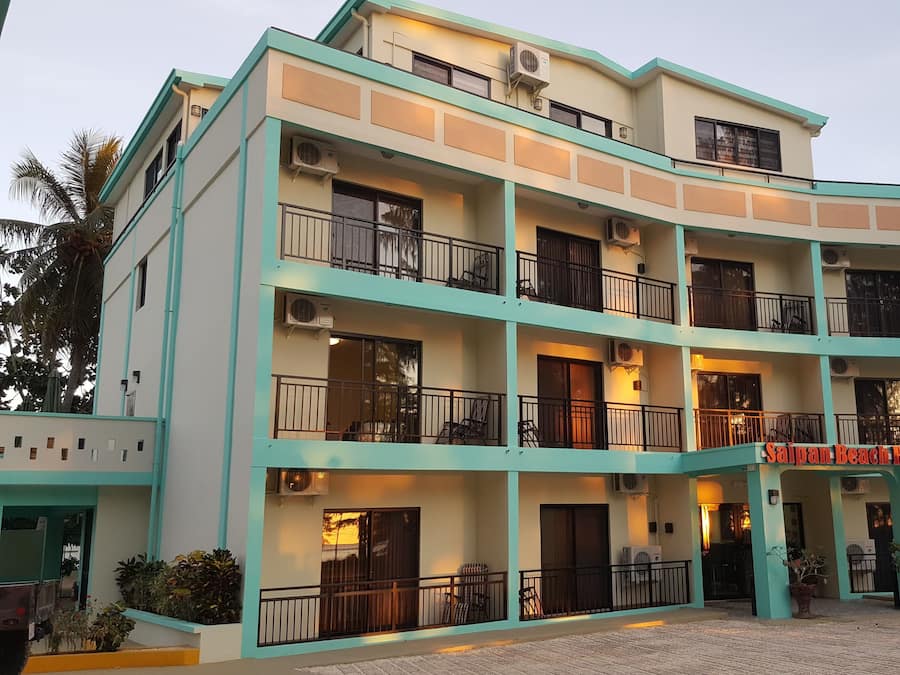 A multi-story hotel with balconies, air conditioning units, and a sign reading "Saipan Beach Hotel".
