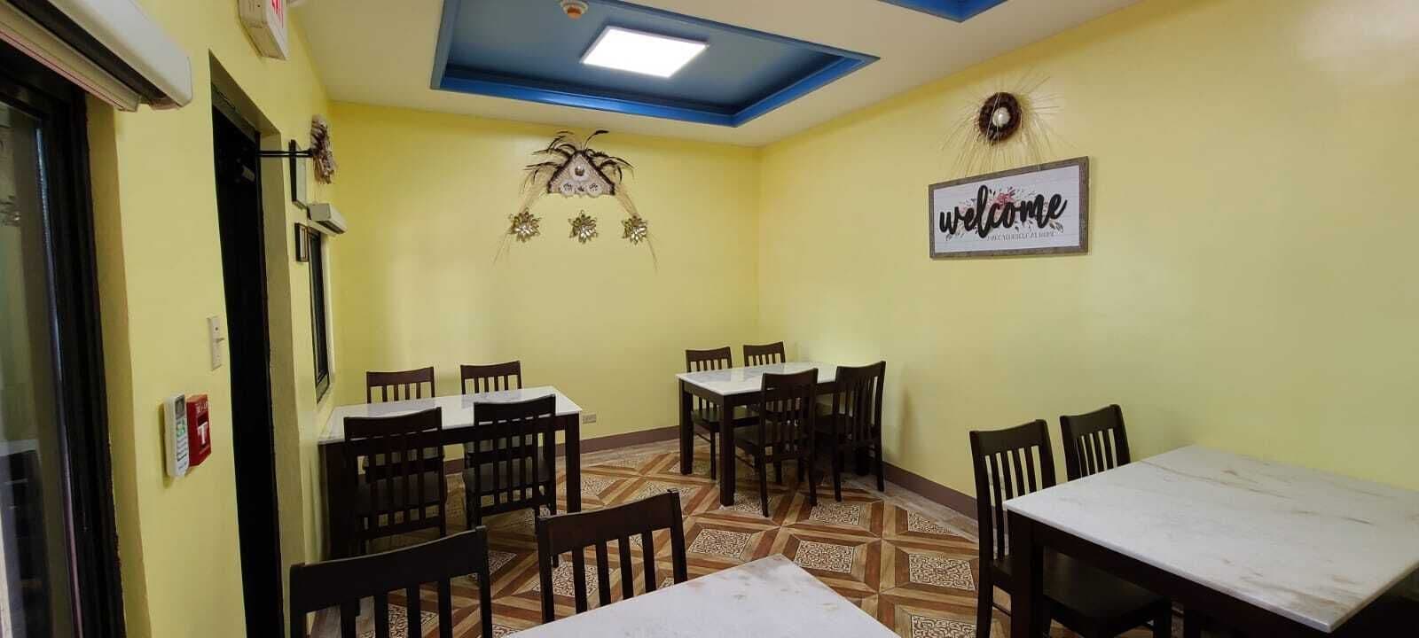 A dining area with tables and chairs, a ceiling light, and a welcome sign on the wall.