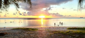 Eine Strandansicht bei Sonnenuntergang, ruhiges Wasser und badende Menschen.