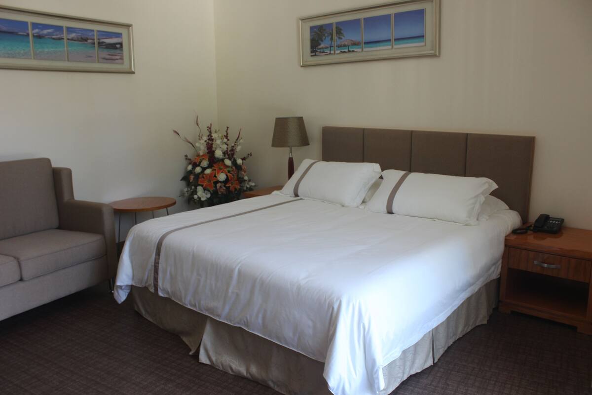 Habitació d'hotel amb un llit, un sofà, una taula de nit amb una làmpada i un vas de flors.