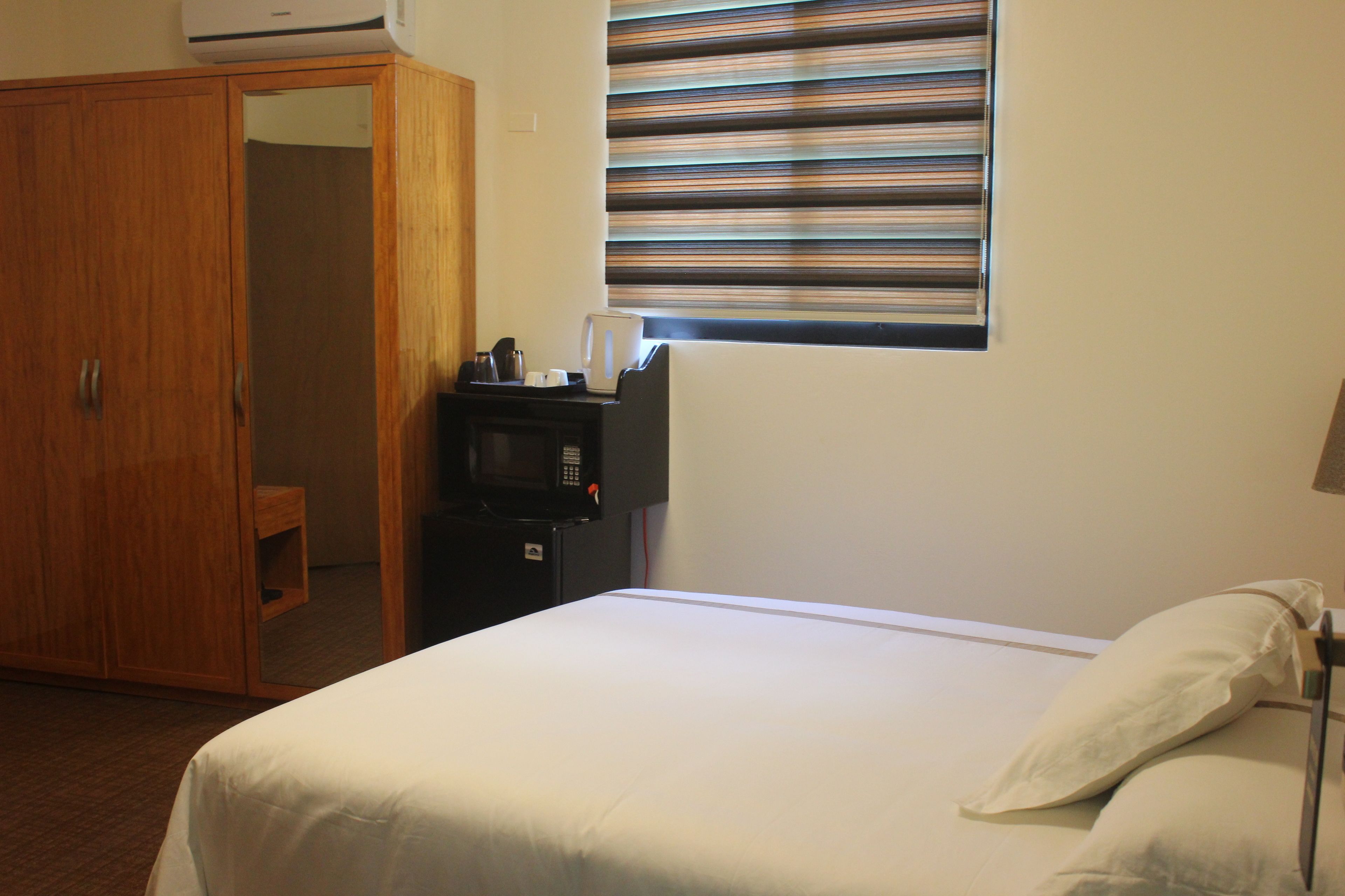 A hotel room with a bed, a wardrobe, a microwave, and a window with blinds.