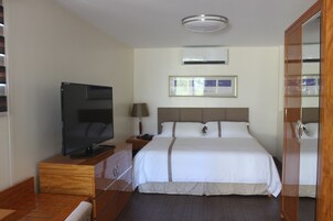 A hotel room with a bed, a television on a wooden dresser, a nightstand with a lamp, and a mirror.