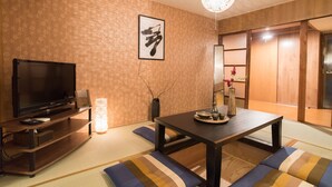 A traditional Japanese room with tatami flooring, a low table with cushions, a television, and a decorative vase. - Ikenoya (Kyoto)