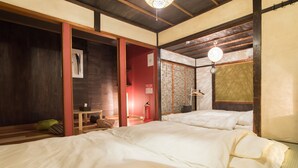 A traditional Japanese-style room with two beds, a small table, and a red door. - Ikenoya (Kyoto)