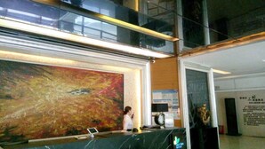 Un área de recepción con un cuadro abstracto de gran tamaño, un mostrador de recepción y una pantalla digital.