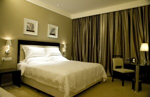A hotel room with a large bed, two wall-mounted lamps, a desk with a chair, and a large window with curtains. - KaiMan Hotel (Zhuhai)