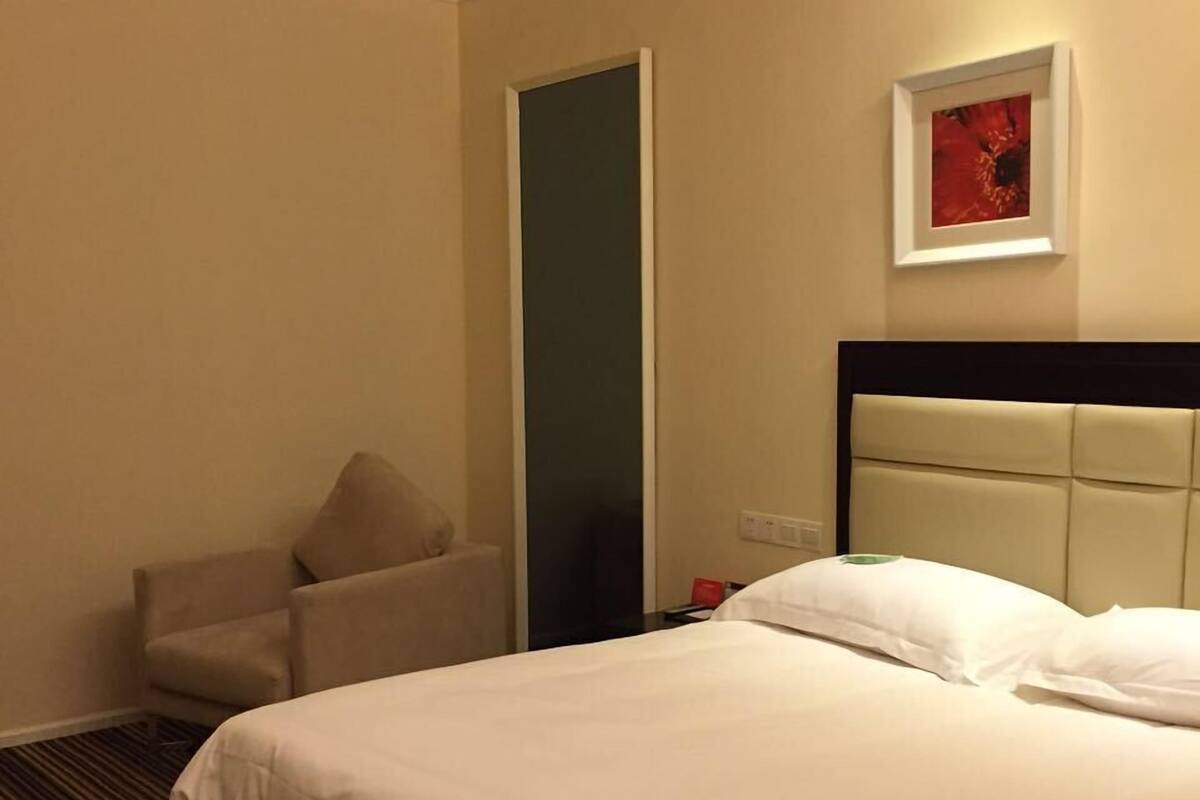 A hotel room with a large bed, a chair, a nightstand, a framed picture on the wall, and a door.