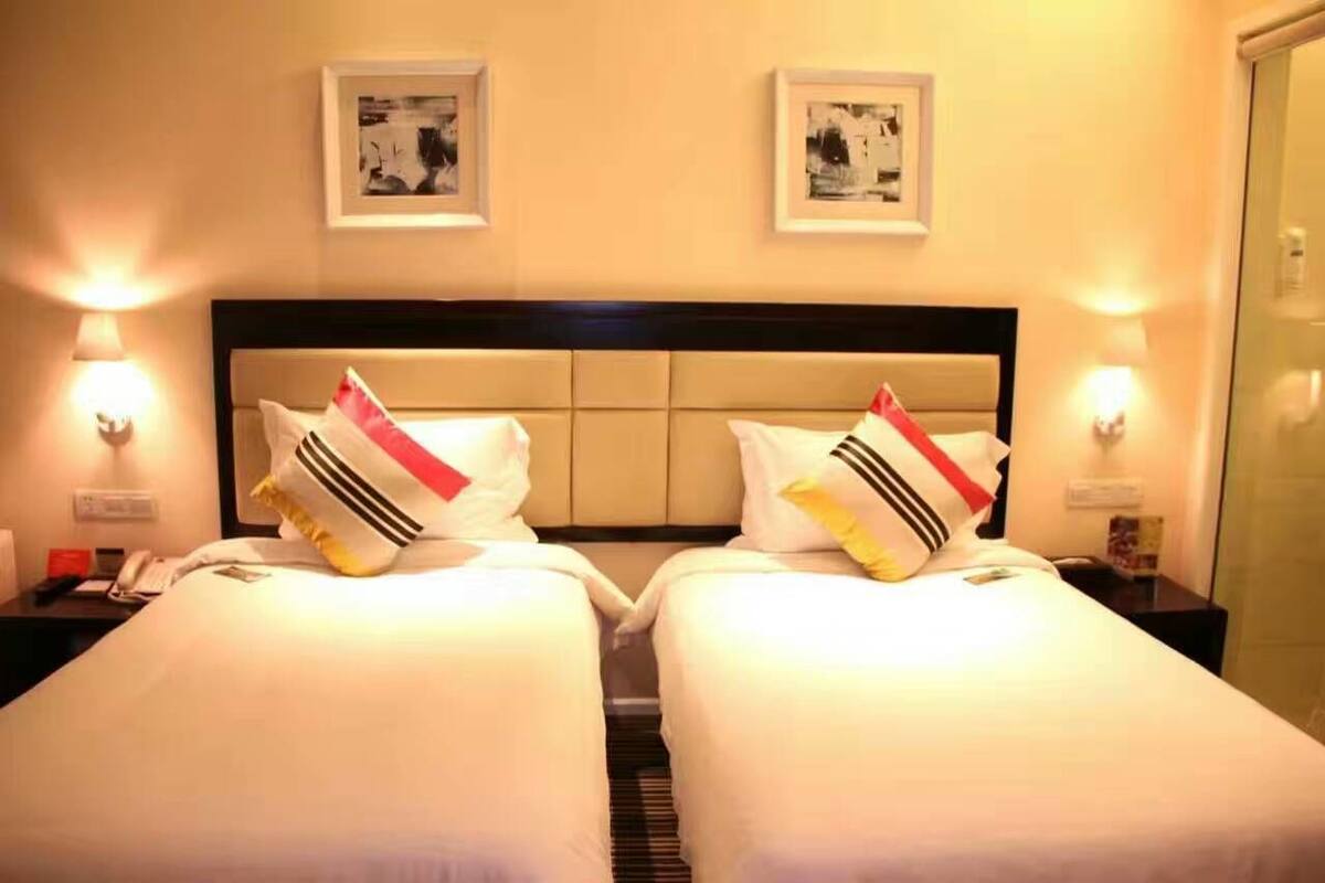 A hotel room with two single beds, each with a headboard and bedside lamps.