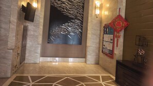 A modern lobby with a large abstract wall art, a reception desk, and a red decorative hanging. - Beijing Yilejia Apartment (Beijing)