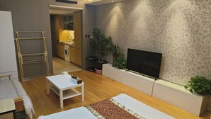 A hotel room with a bed, a small table, a TV, and a kitchen area in the background. - Beijing Yilejia Apartment (Beijing)