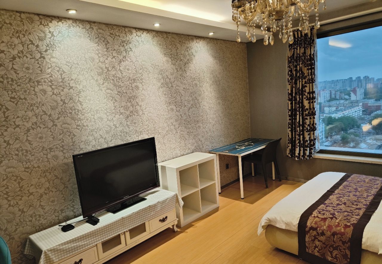A hotel room with a TV, a small desk, a bed, and a view of the city.