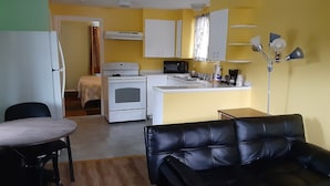 A compact living space with a kitchenette, a dining area with a table and chairs, a black leather sofa, and a bed with a patterned bedspread. - Shiny Motel (Hoquiam)